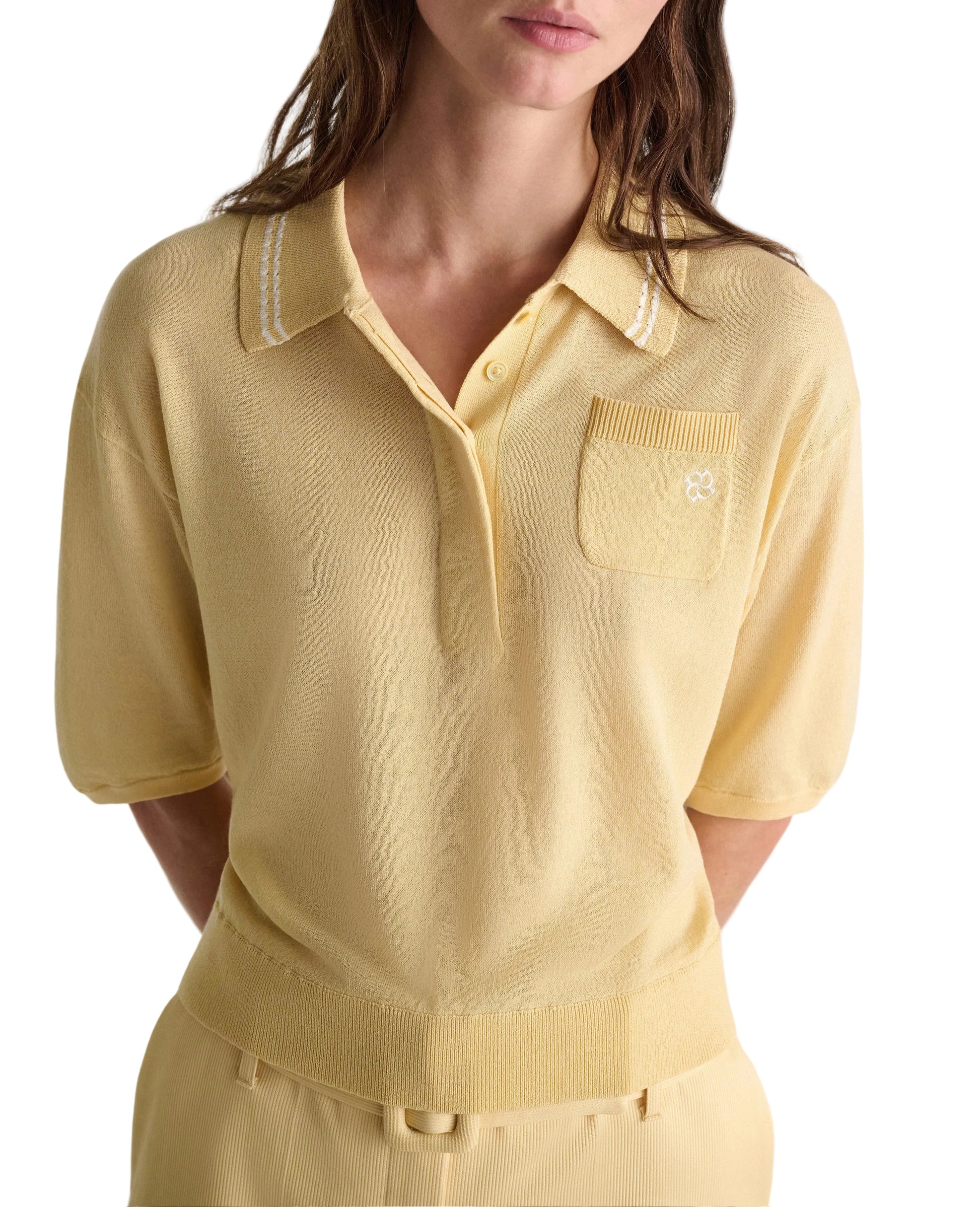 A woman wearing the Dorothee Schumacher Refined Essentials Pullover, a light yellow stretch cotton top with collar, chest pocket, and ribbed waist detail, paired with matching trousers.