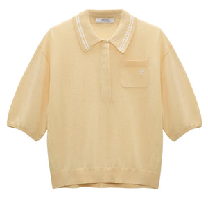 The Refined Essentials Pullover by Dorothee Schumacher is a light yellow short-sleeve polo in stretch cotton, featuring a collar, front buttons, small chest pocket, and a subtle embroidered logo on the pocket.