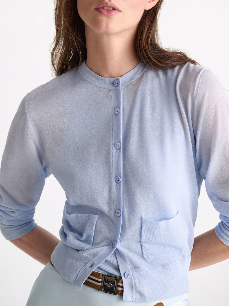 A woman shown from shoulders to hips wears the Dorothee Schumacher Sheer Summer Twinset—a light blue cropped stretch cotton cardigan with two front pockets—paired with light-colored pants.