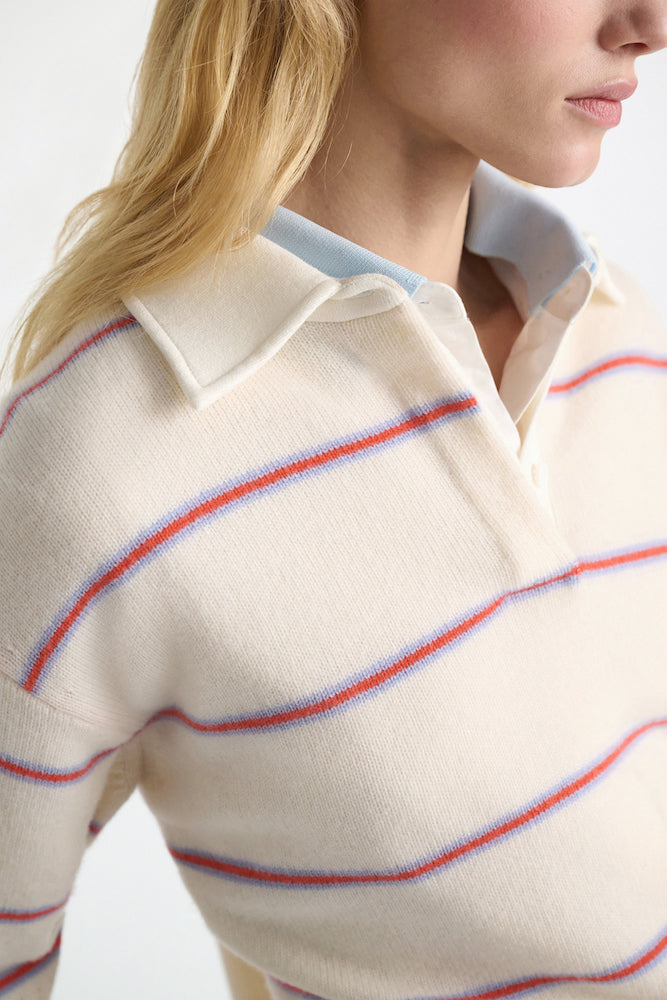 A person wears the Sporty Statements Pullover by Dorothee Schumacher, a cream Merino-cashmere knit with blue and red stripes, layered over a collared shirt for a cropped, boxy look.