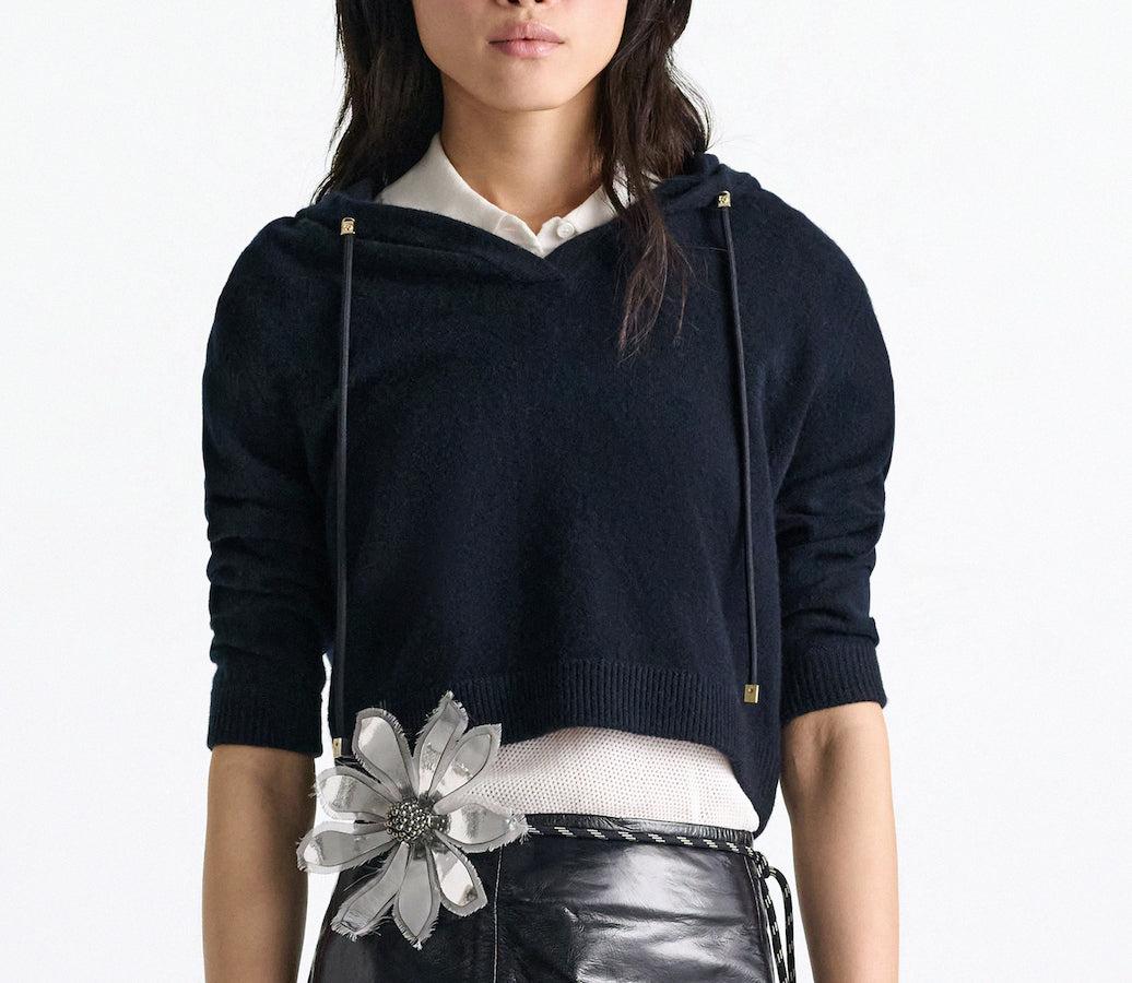 A woman wears the Dorothee Schumacher Modern Statements Pullover over a white collared shirt, paired with a black leather skirt featuring a bold silver flower accent at the waist.