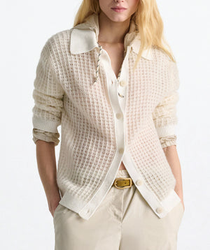 A woman wears the Dorothee Schumacher Airy Softness Cardigan—cream-colored, alpaca-wool blend with button front—over a collared shirt and beige pants, standing against a white background.