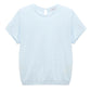 The Natural Ease Shirt by Dorothee Schumacher is a light blue heathered top with short sleeves, a crew neck, and a small buttoned keyhole at the back neckline, shown against a plain white background.
