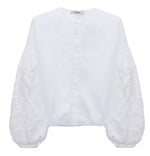 The Embroidered Beauty Blouse by Dorothee Schumacher is a white cotton top with a round neckline, long balloon sleeves, and detailed floral embroidery.