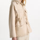 A woman wears the Dorothee Schumacher Emotional Essence Jacket in light beige with flap pockets and a drawstring waist, paired with matching Punto Milano pants, standing against a plain white background.