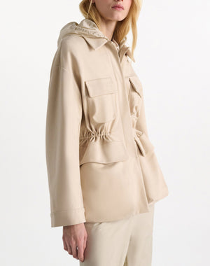 A woman wears the Dorothee Schumacher Emotional Essence Jacket in light beige with flap pockets and a drawstring waist, paired with matching Punto Milano pants, standing against a plain white background.