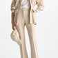 A woman wears Dorothee Schumacher's Emotional Essence Pants with a beige utility jacket, white top, heeled sandals, and holds a beige baseball cap in her left hand.