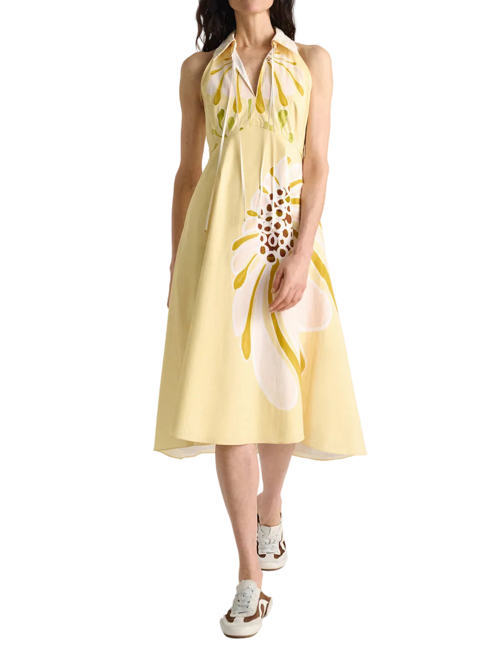 A woman wears the Dorothee Schumacher Floral Power Dress—a light yellow, white and yellow floral cotton poplin midi-dress with a removable lace collar—paired with white sneakers.