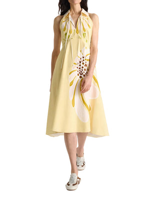 A woman wears the Dorothee Schumacher Floral Power Dress—a light yellow, white and yellow floral cotton poplin midi-dress with a removable lace collar—paired with white sneakers.