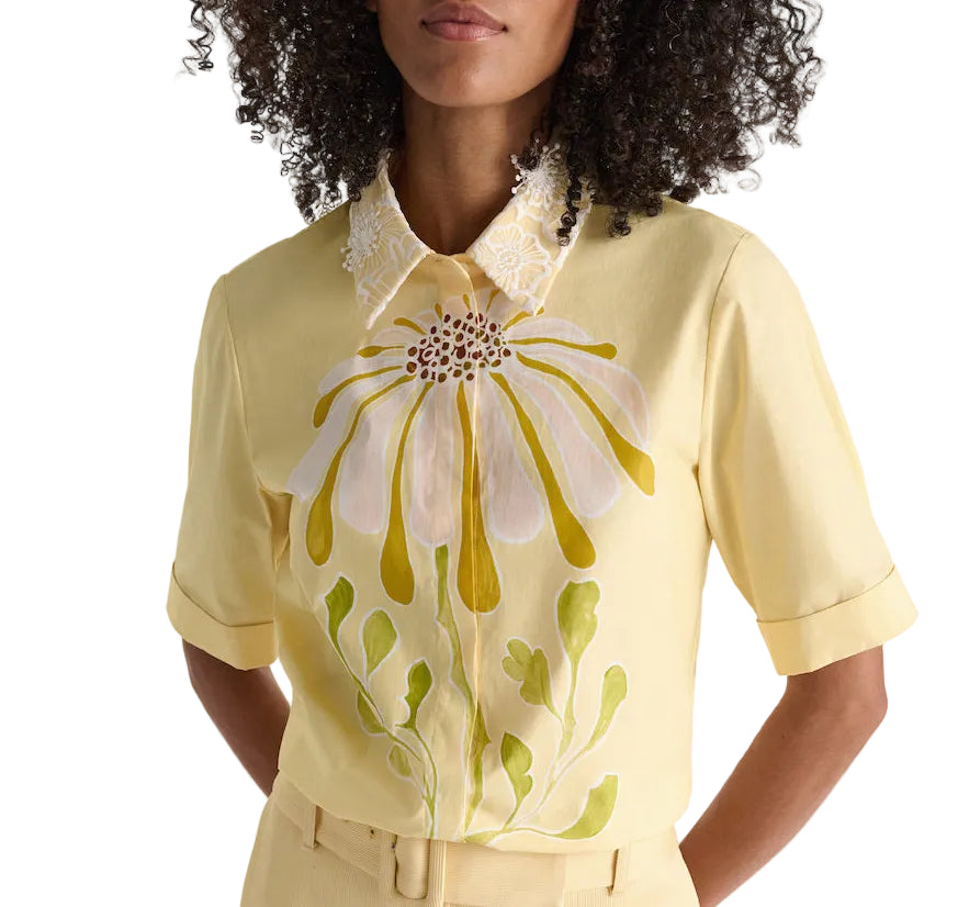 Woman wears the Floral Power Blouse by Dorothee Schumacher, a light yellow cotton poplin top with a bold front floral design and a removable lace collar for versatile styling.