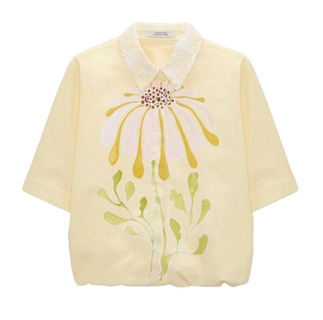 The Floral Power Blouse by Dorothee Schumacher is a light yellow cotton poplin top featuring a removable lace collar and a bold pastel pink, yellow, and green floral design on the front.