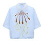 Dorothee Schumacher’s Floral Power Blouse in light blue cotton poplin features short sleeves, a removable lace collar, and bold abstract floral prints in brown, blue, and green on the front.