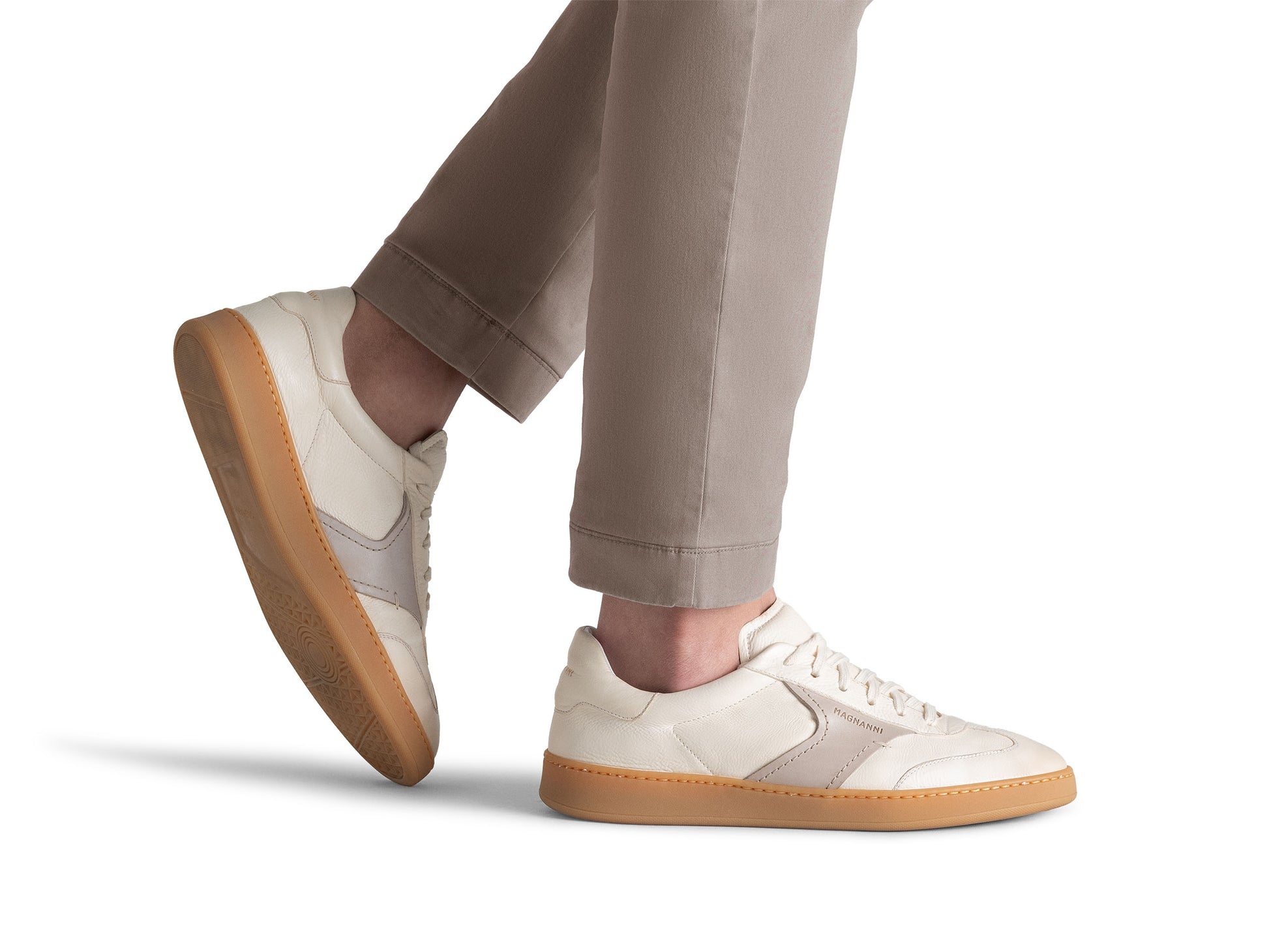 A person wears beige pants and the Magnanni Zori Sneaker, featuring a leather upper and tan gum soles, shown from the lower legs down against a white background.