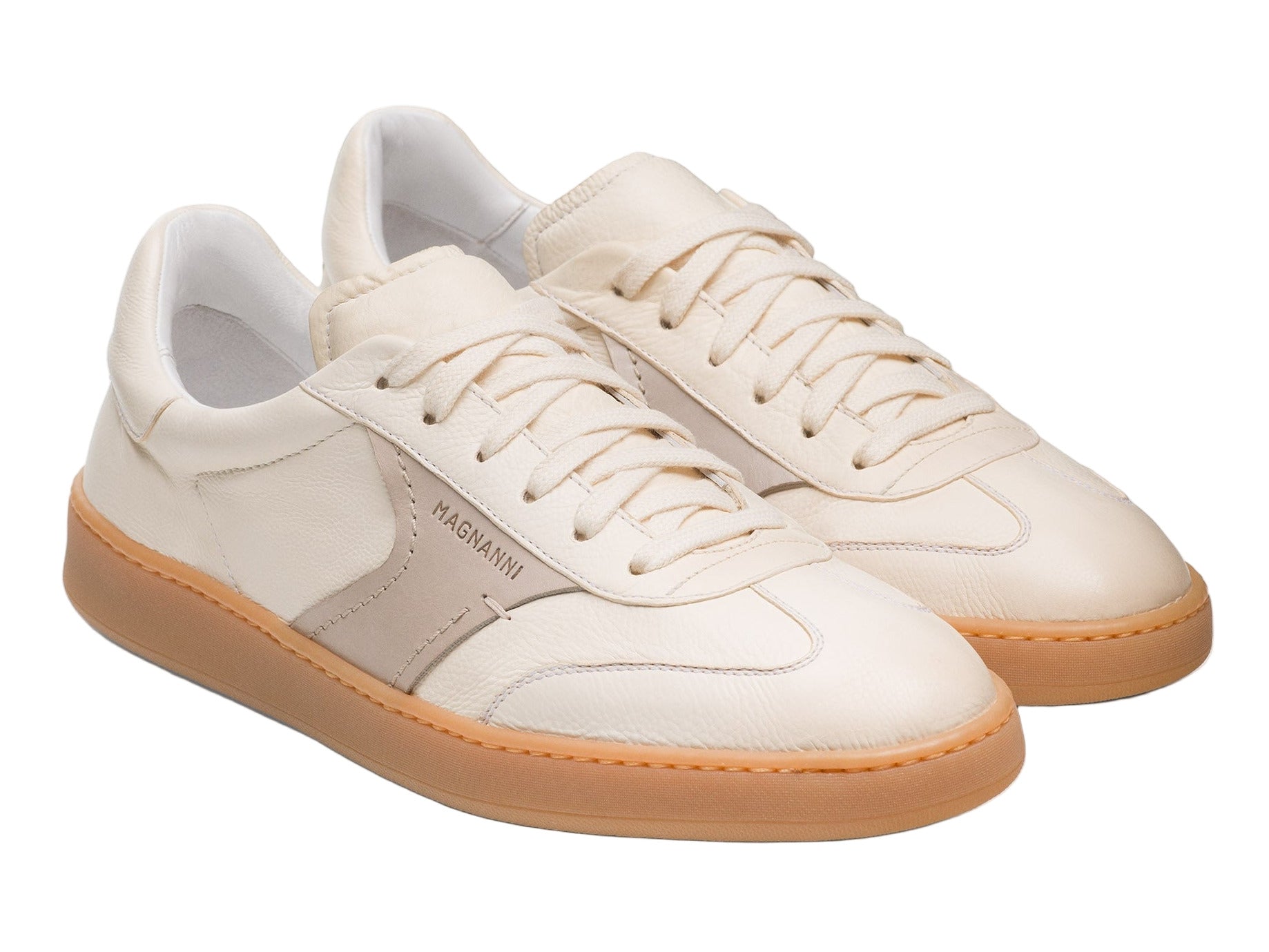 The Zori Sneaker by Magnanni features an off-white premium leather upper, tan rubber sole, white laces, and "MAGNANNI" on the side—blending everyday style with versatile comfort.