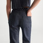 A person in Dorothee Schumacher's Fluid Denim Pants and a sleeveless dark denim braided-detail top, seen from the back with one hand in their pocket.