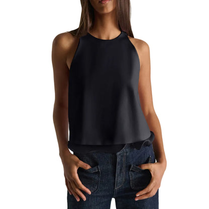 A woman models the Dorothee Schumacher Emotional Essence Top, a sleeveless black design with a subtle georgette hem, paired with dark blue jeans, standing against a white background with her hands in her pockets.