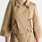 A person wears the Dorothee Schumacher Luxury Layer Jacket in beige, featuring 3/4 sleeves, large angled front pockets, and button details. The photo is cropped from chin to mid-thigh.