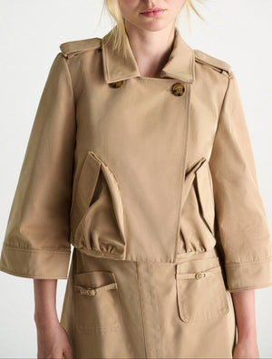 A person wears the Dorothee Schumacher Luxury Layer Jacket in beige, featuring 3/4 sleeves, large angled front pockets, and button details. The photo is cropped from chin to mid-thigh.