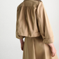 The Luxury Layer Jacket by Dorothee Schumacher is styled over a tan trench coat, shown from the back against a plain light background.