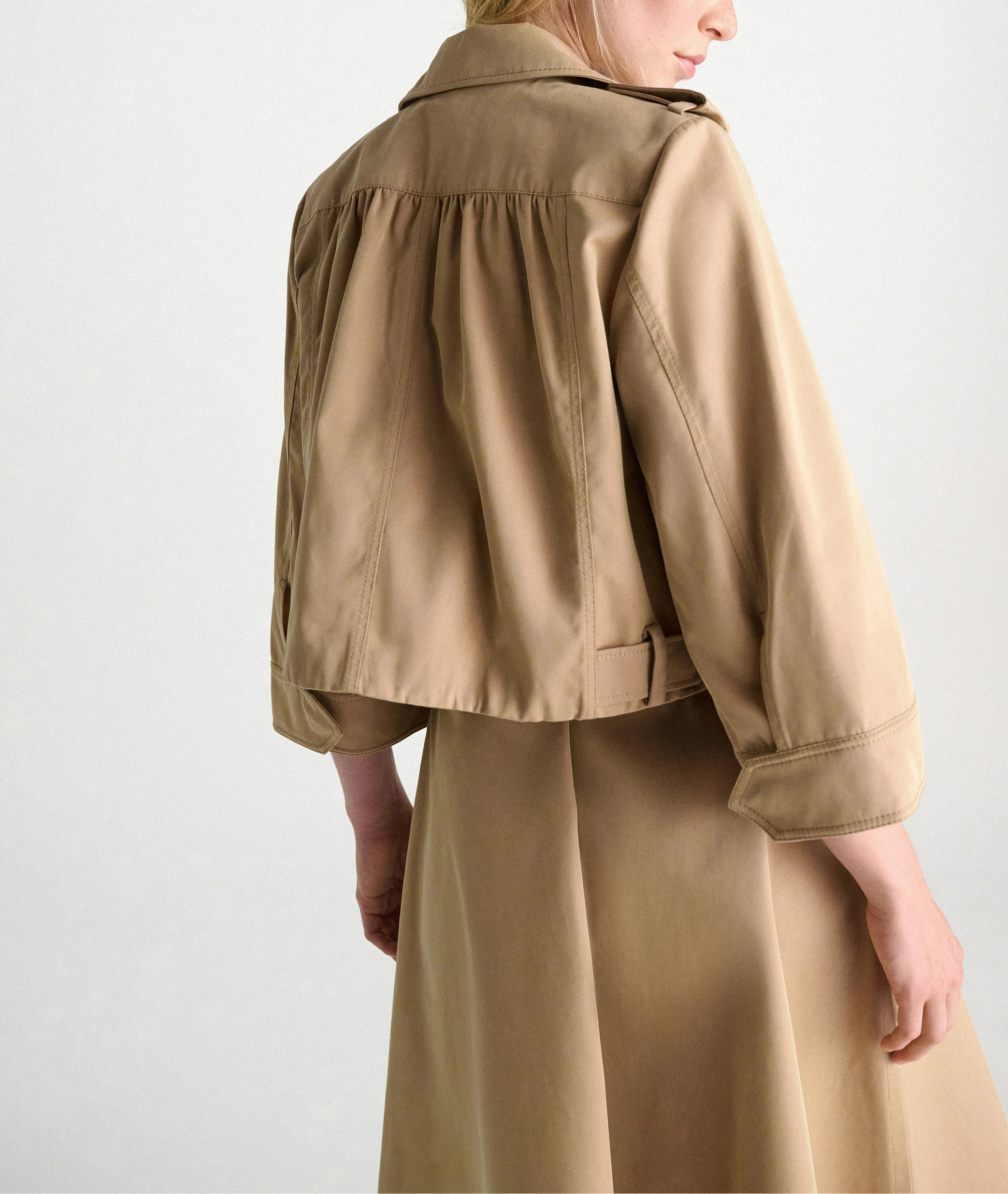 The Luxury Layer Jacket by Dorothee Schumacher is styled over a tan trench coat, shown from the back against a plain light background.