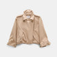 The Dorothee Schumacher Luxury Layer Jacket is a beige cropped cotton design featuring wide lapels, button accents, flap pockets, and long sleeves, shown against a plain white background.