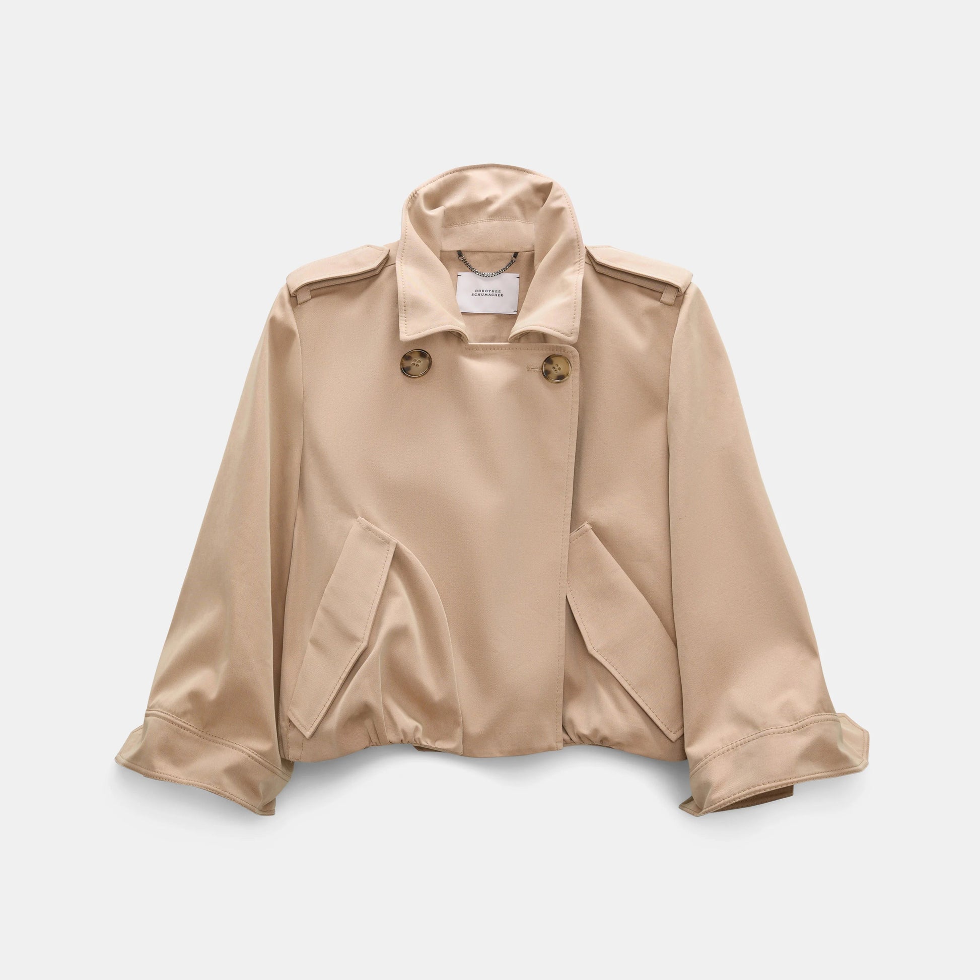 The Dorothee Schumacher Luxury Layer Jacket is a beige cropped cotton design featuring wide lapels, button accents, flap pockets, and long sleeves, shown against a plain white background.