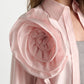 A woman wears the Dorothee Schumacher Striped Power Blouse, featuring a light pink oversized fit and a sculpted rose-shaped shoulder detail, styled over a gray ribbed top.