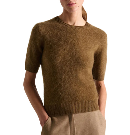 A person wears the Dorothee Schumacher Fluffy Statements Pullover—a short-sleeve, extra-soft sweater—paired with beige pants and hands in pockets, standing against a white background for a cozy, layered look perfect for any season.