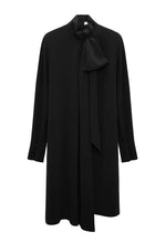 The Statement Drape Dress by Dorothee Schumacher is a long-sleeve black dress made from luxurious Japanese crepe, showcasing a high neckline with a dramatic bow detail at the neck, set against a plain white background.