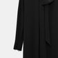 The Statement Drape Dress by Dorothee Schumacher is a long-sleeved black Japanese crepe dress featuring a high neckline and a large bow detail near the collar, displayed against a plain background.