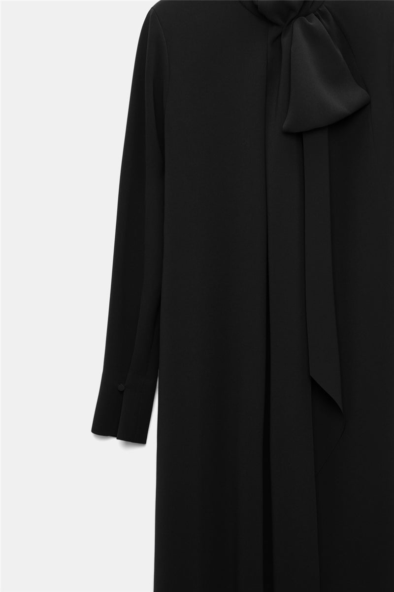 The Statement Drape Dress by Dorothee Schumacher is a long-sleeved black Japanese crepe dress featuring a high neckline and a large bow detail near the collar, displayed against a plain background.