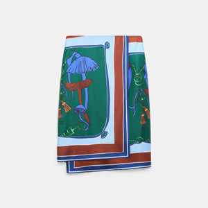 The Cosmic Funghi Skirt by Dorothee Schumacher features a vibrant botanical mushroom print in blue, green, brown, and orange hues. Its rectangular silhouette and contrasting double border evoke the look of a silk twill scarf with a layered hemline, shown laid flat against a plain background.