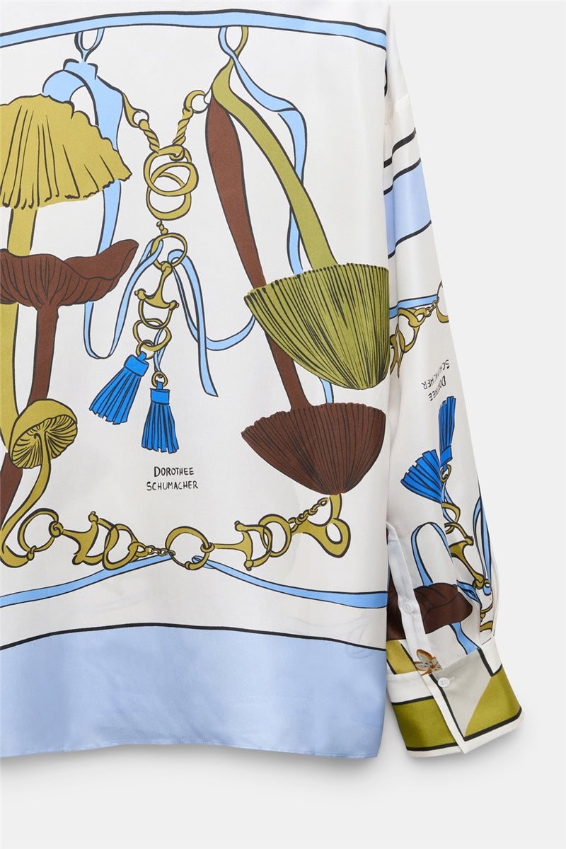 Introducing the Cosmic Funghi Blouse by Dorothee Schumacher—an oversized silk twill blouse adorned with blue, green, and brown abstract shapes, gold chain motifs, and tassel details. The fabric features "Dorothee Schumacher" text subtly printed throughout, making a statement with its elegant drape and distinctive design.