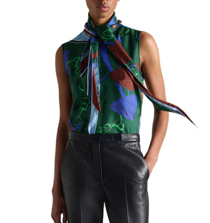 A model wears the Dorothee Schumacher Cosmic Funghi Top—a sleeveless blouse featuring a tie collar and green mushroom print—paired with black leather pants, standing with one hand in her pocket against a white background.