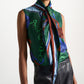 A person is wearing the Dorothee Schumacher Cosmic Funghi Top, a sleeveless blouse featuring a tie collar and a green printed pattern, paired with high-waisted black leather pants and shown from shoulders to hips.