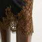 Close-up of the Dorothee Schumacher Shiny Statement Skirt, a black technical satin midi-skirt with brown lace trim at the hem, styled over brown leather pants.