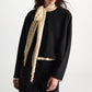 A person stands against a plain background wearing the Dorothee Schumacher Emotional Essence Blouse—an oversized black long-sleeve blouse paired with pants. A light beige sheer scarf is tied in a bow closure around their neck.