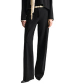 A person is seen wearing the Dorothee Schumacher Emotional Essence Pants—black wide-leg trousers with an unfinished hemline—styled with a black long-sleeve top and black shoes, standing with arms relaxed at their sides. The image is cropped below the shoulders against a white background.