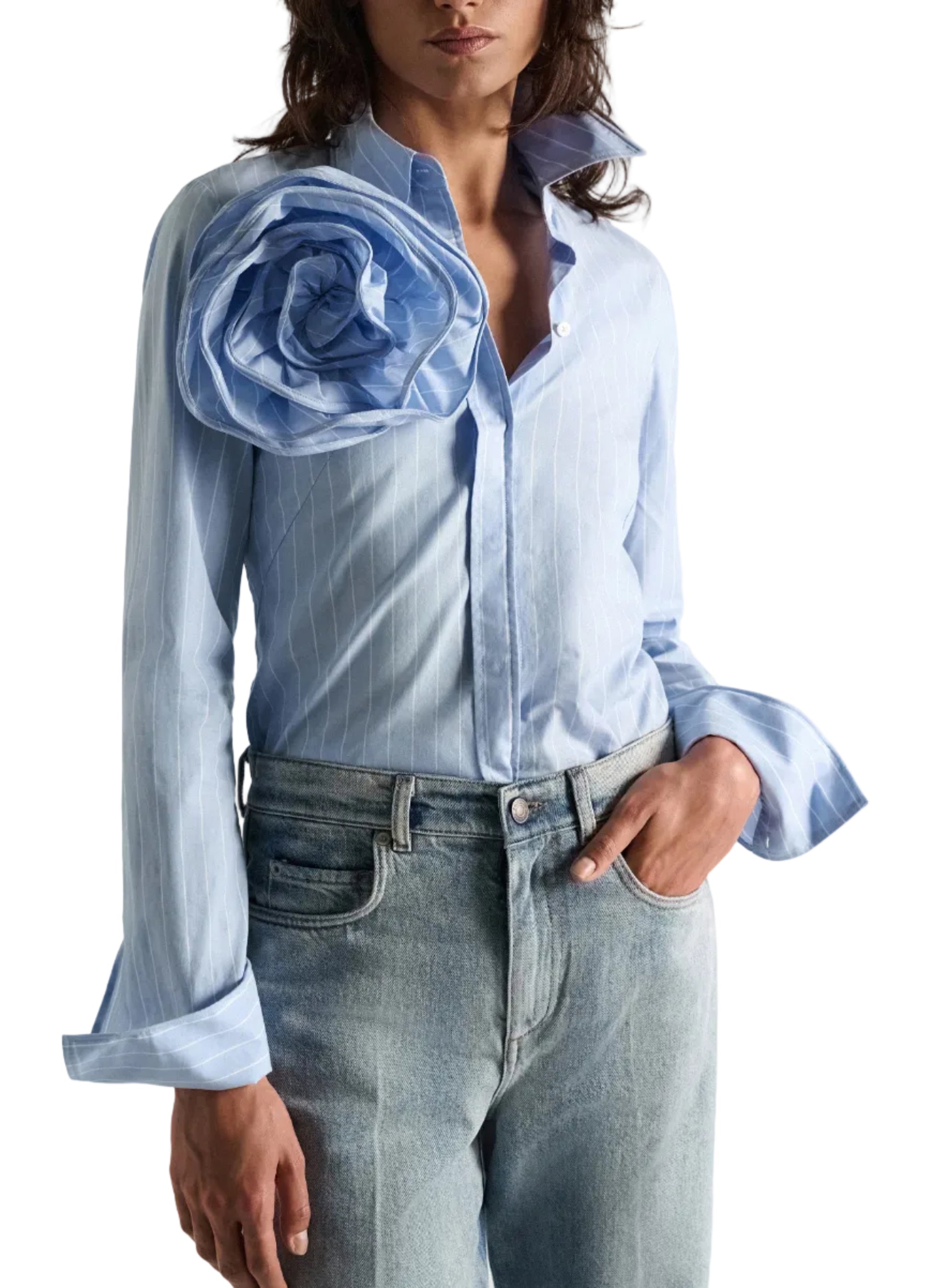 A person wearing the Dorothee Schumacher Striped Power Blouse—a light blue cotton poplin shirt featuring stripes, a large fabric flower on one shoulder, and flared cuffs—paired with light wash jeans.