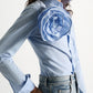 A model wears the Striped Power Blouse by Dorothee Schumacher, crafted from soft cotton poplin in light blue stripes and adorned with a prominent rose brooch on the chest, paired with light blue jeans.