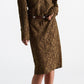 A woman wearing the DS Powerful Lace Dress by Dorothee Schumacher—a brown guipure lace shirtdress featuring long sleeves, a collar, and a dark belt—pairs it with taupe heeled sandals as she stands against a plain white background.