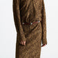 A person wearing the DS Powerful Lace Dress by Dorothee Schumacher—a long-sleeved, brown guipure lace shirtdress with a collar and a brown belt featuring metallic accents—stands against a plain background.