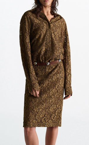 A person wearing the DS Powerful Lace Dress by Dorothee Schumacher—a long-sleeved, brown guipure lace shirtdress with a collar and a brown belt featuring metallic accents—stands against a plain background.