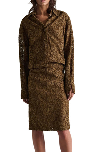 A person wearing the DS Powerful Lace Dress by Dorothee Schumacher—a brown guipure lace shirtdress featuring an elastic waist and a matching knee-length skirt—shown from the knees up.