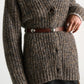 Person wearing a chunky, brown knit cardigan with buttons, belted at the waist with the Dorothee Schumacher True Cuoio Stud Belt—a thin belt featuring a stylish pin stud closure—and a black skirt underneath.