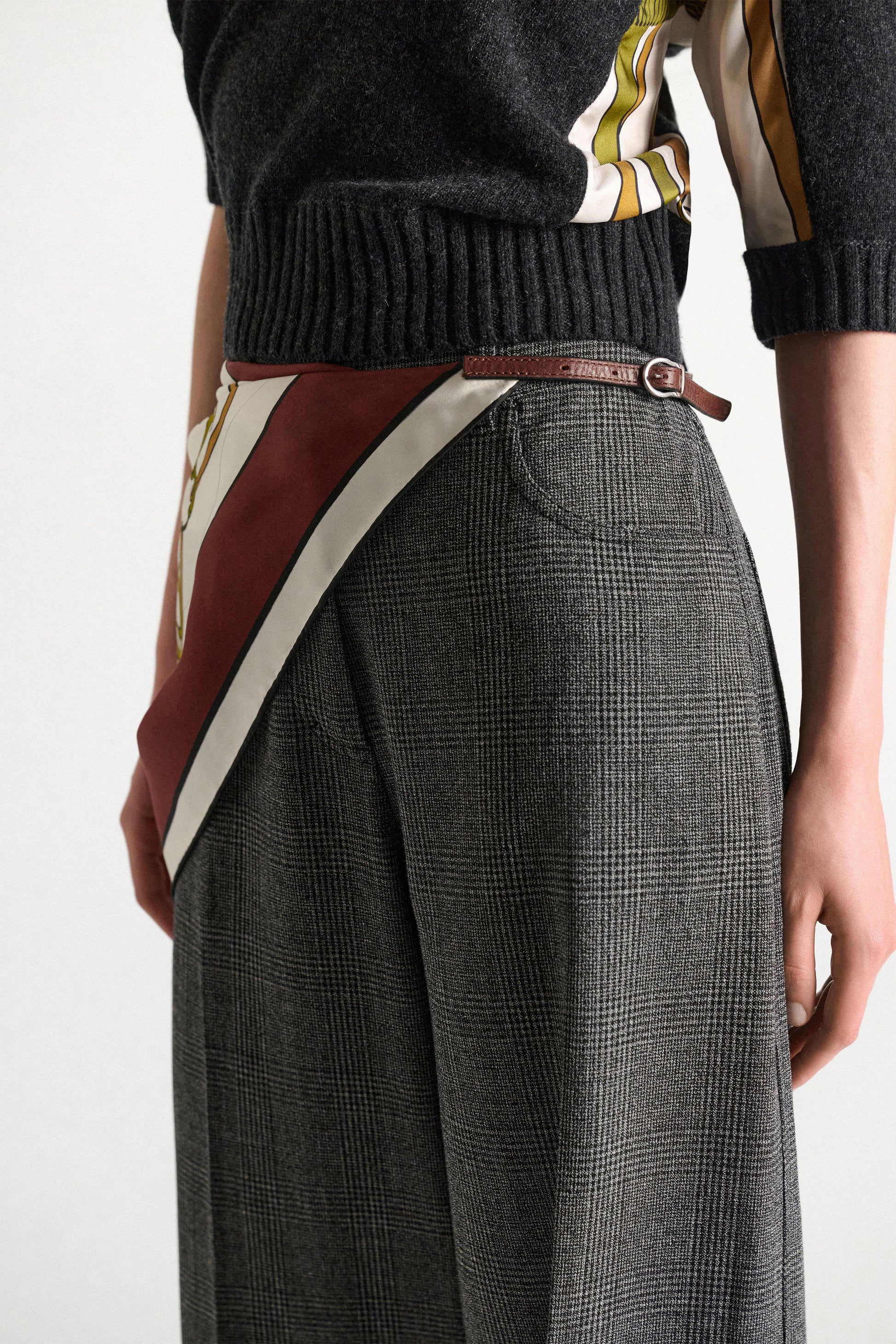 A person is wearing a dark sweater, high-waisted plaid trousers, and a signature print scarf—secured at the waist with the Dorothee Schumacher Cuoio Softness Scarf Belt. The image is cropped from the shoulders to mid-thigh.