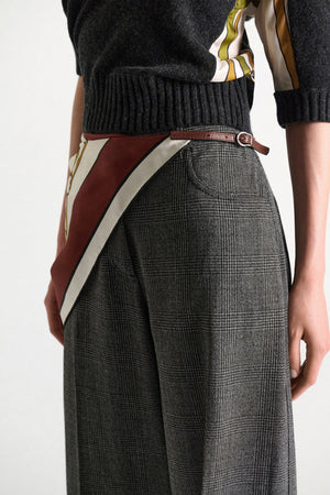 A person is wearing a dark sweater, high-waisted plaid trousers, and a signature print scarf—secured at the waist with the Dorothee Schumacher Cuoio Softness Scarf Belt. The image is cropped from the shoulders to mid-thigh.