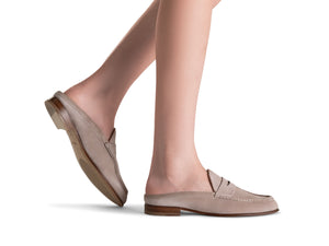 A person wearing the Magnanni Carissa Suede Mule Penny in light beige stands on a white background, highlighting the elegance of this classic women's slip-on mule loafer with wooden soles.