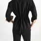 Back view of a person wearing a shimmering Merino-Lurex Shimmering Merino Cardigan with a self-tie sash and rolled tan cuffs, paired with matching black trousers.
