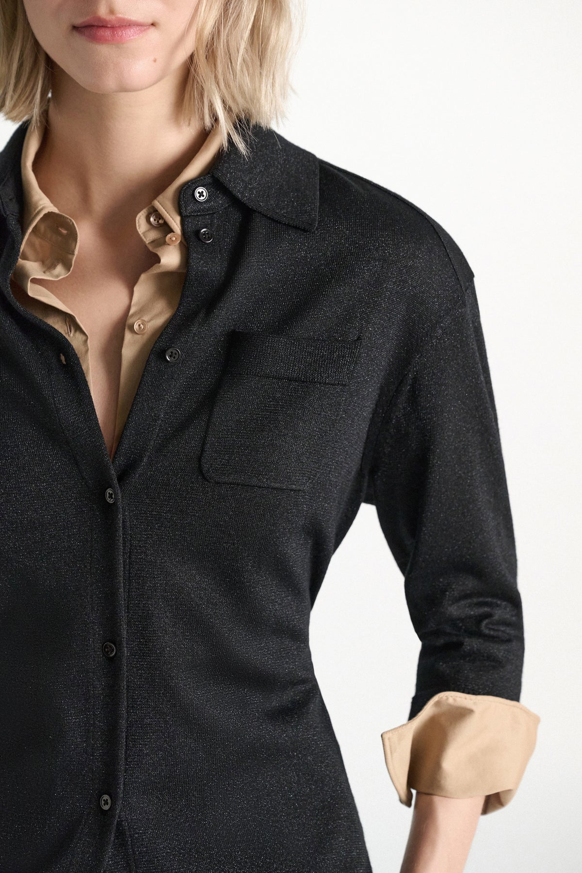 A black Dorothee Schumacher Shimmering Merino Cardigan with a chest pocket and self-tie sash, worn over a beige collared shirt with turned-up cuffs.